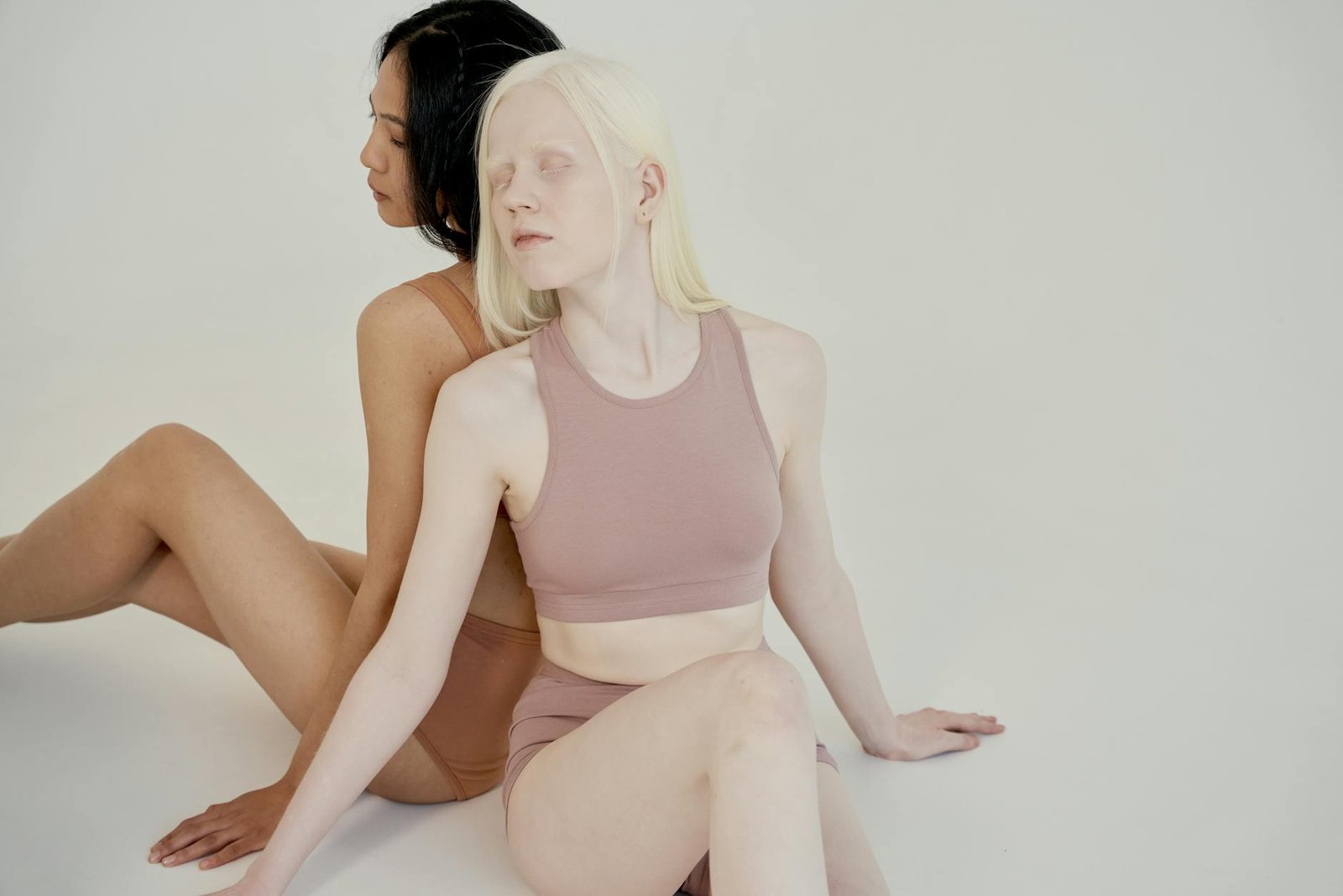 Two diverse women posing back to back in a minimalist studio environment.